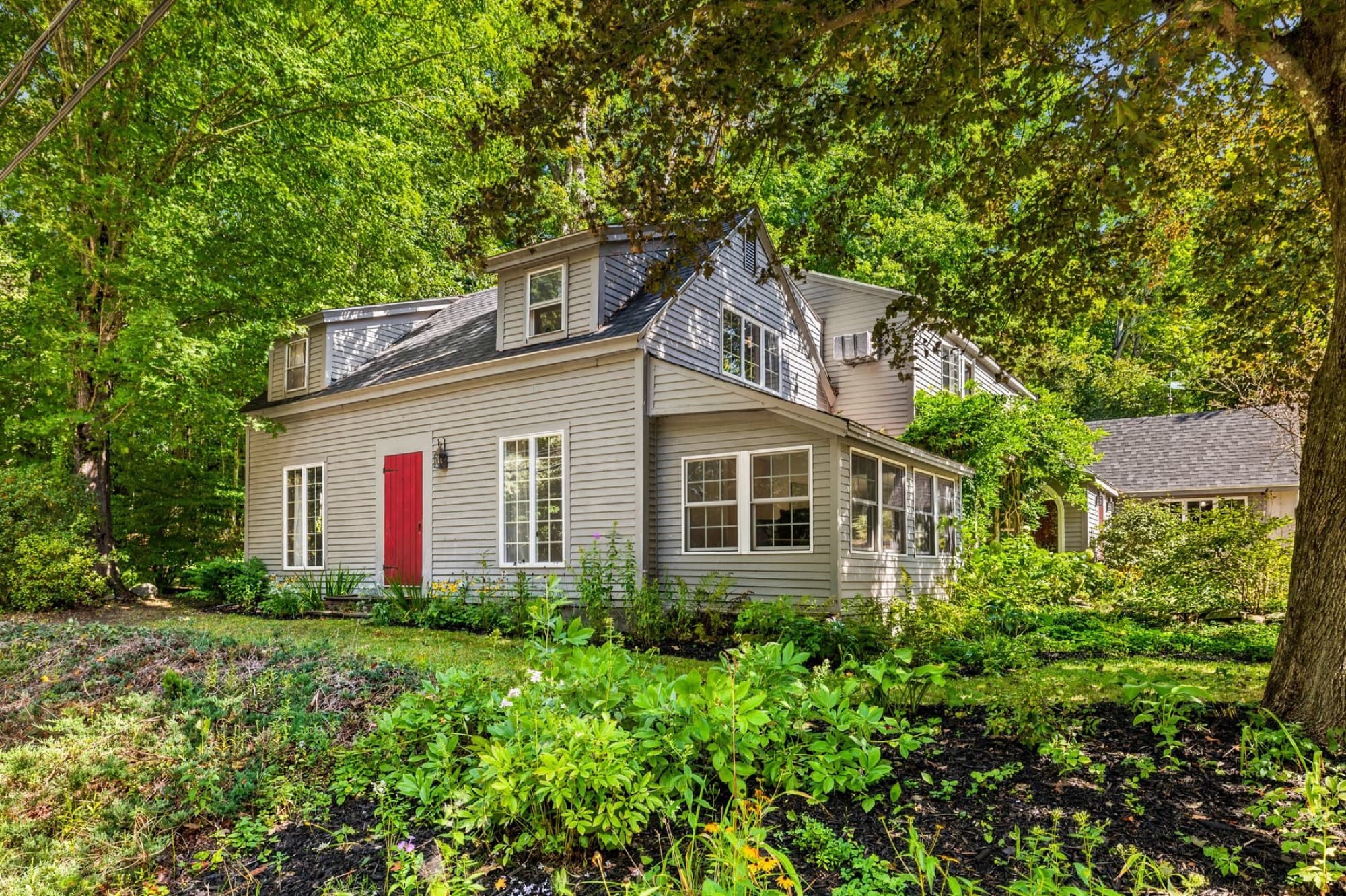 The gray clapboard farmhouse with its red door, seen from the road through the gardens