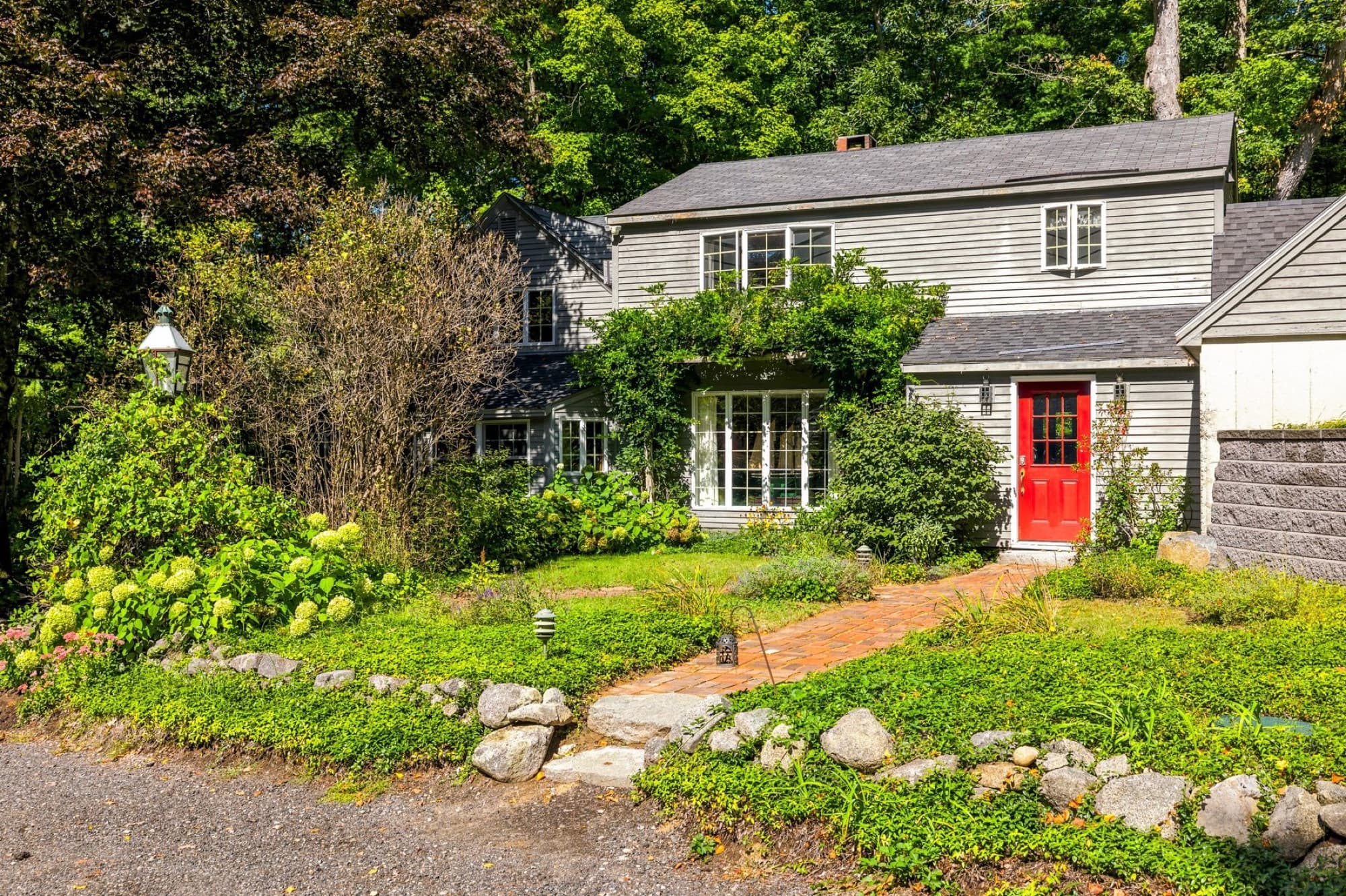 The front of the house with the red door, a brick walkway, and stone-edged garden beds