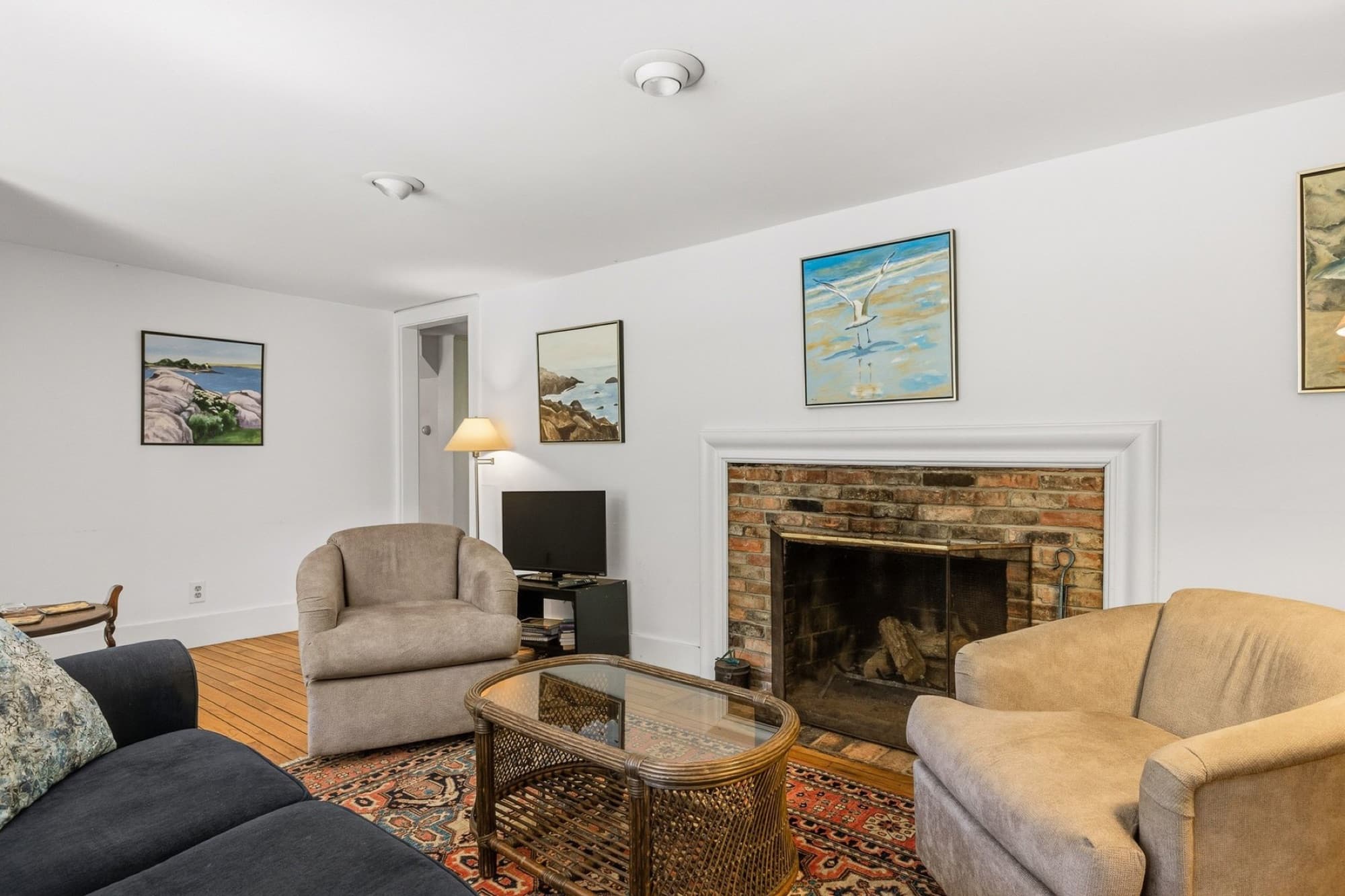 The living room with the brick fireplace, hardwood floors, and an oriental rug