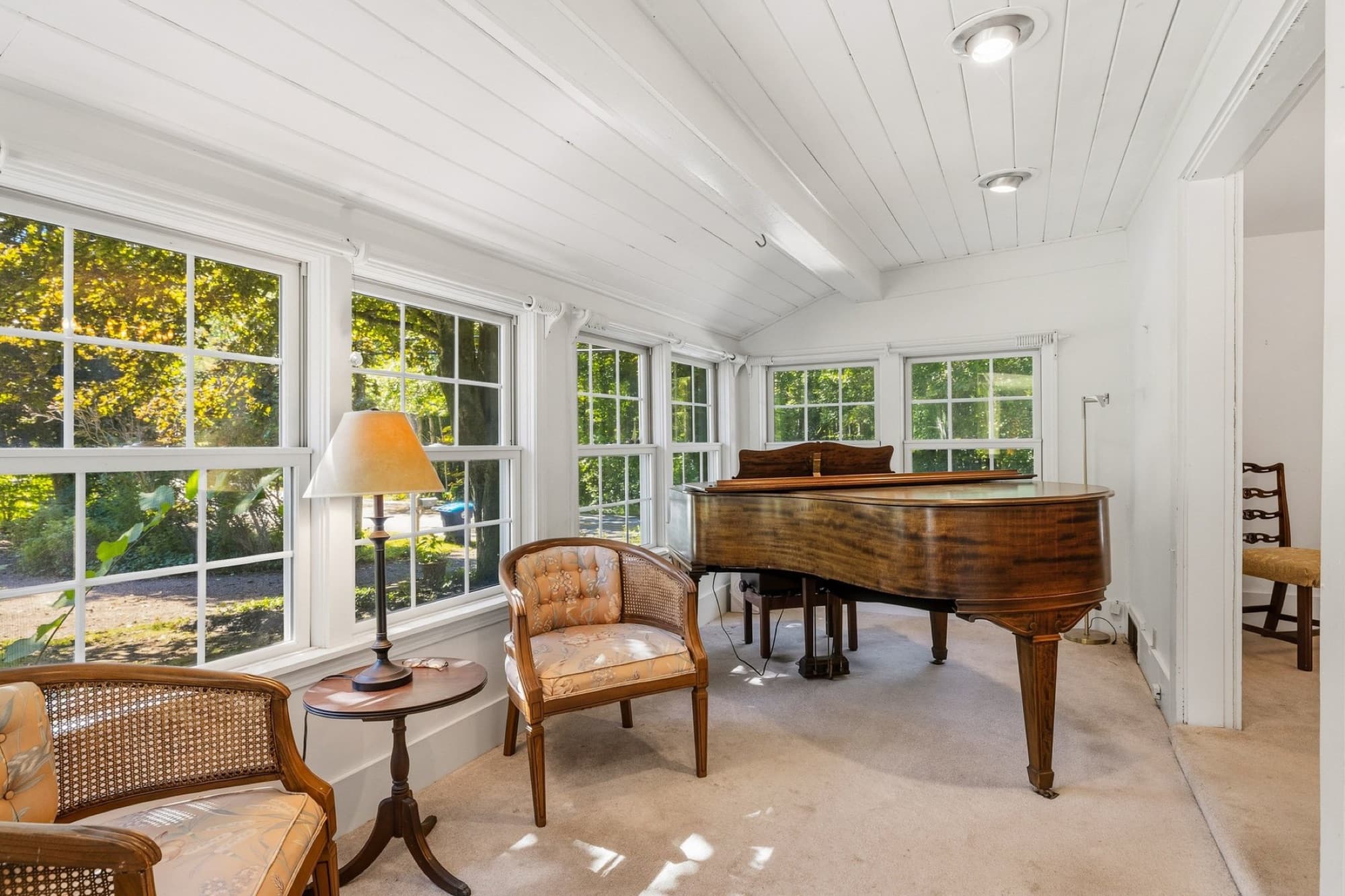The sunroom with a planked ceiling, windows on 3 sides, and a grand piano