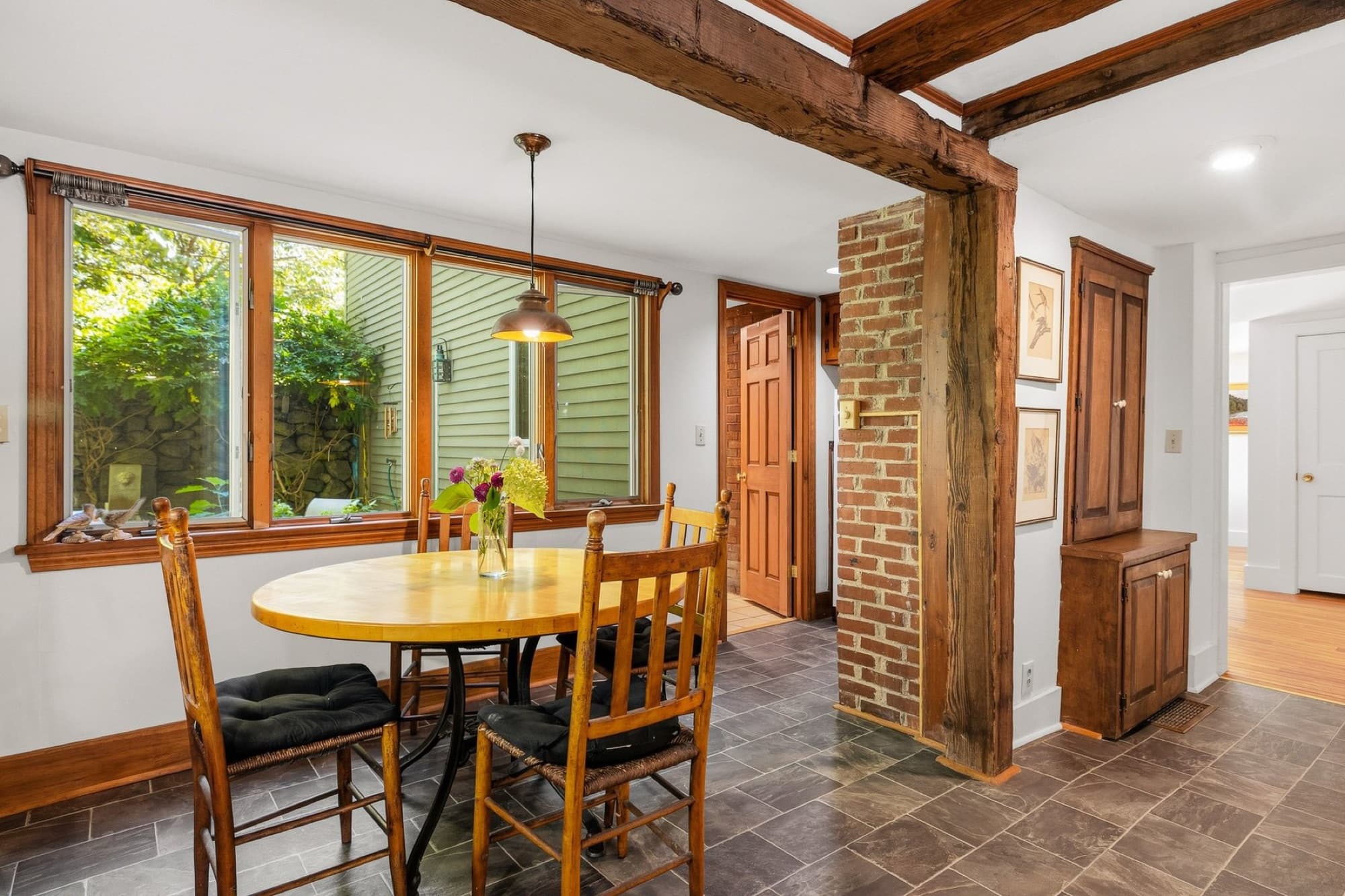 The kitchen table under a pendant light, with windows to the trees