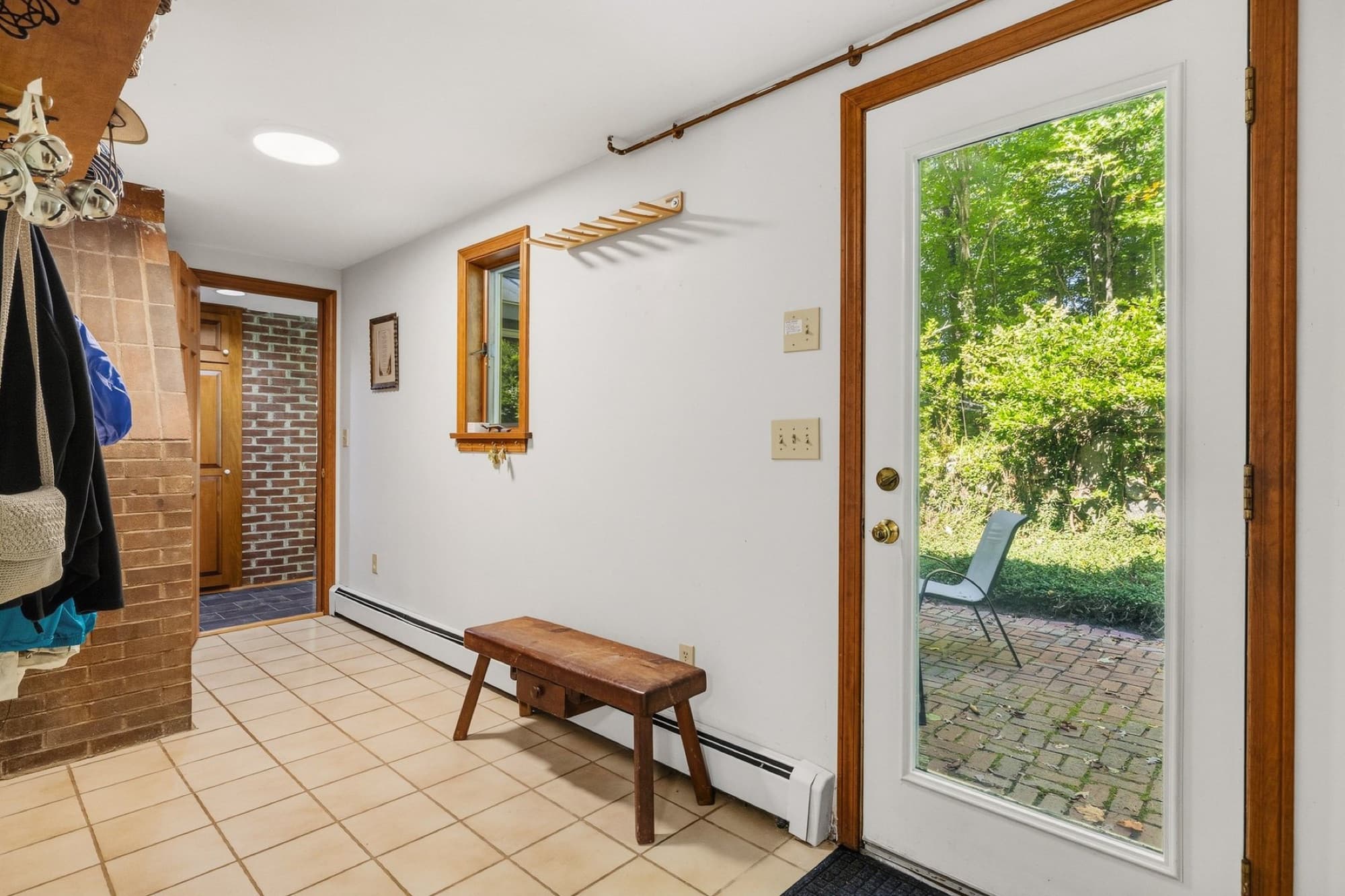 The back entry with a tile floor, a bench, and a glass door to the brick patio