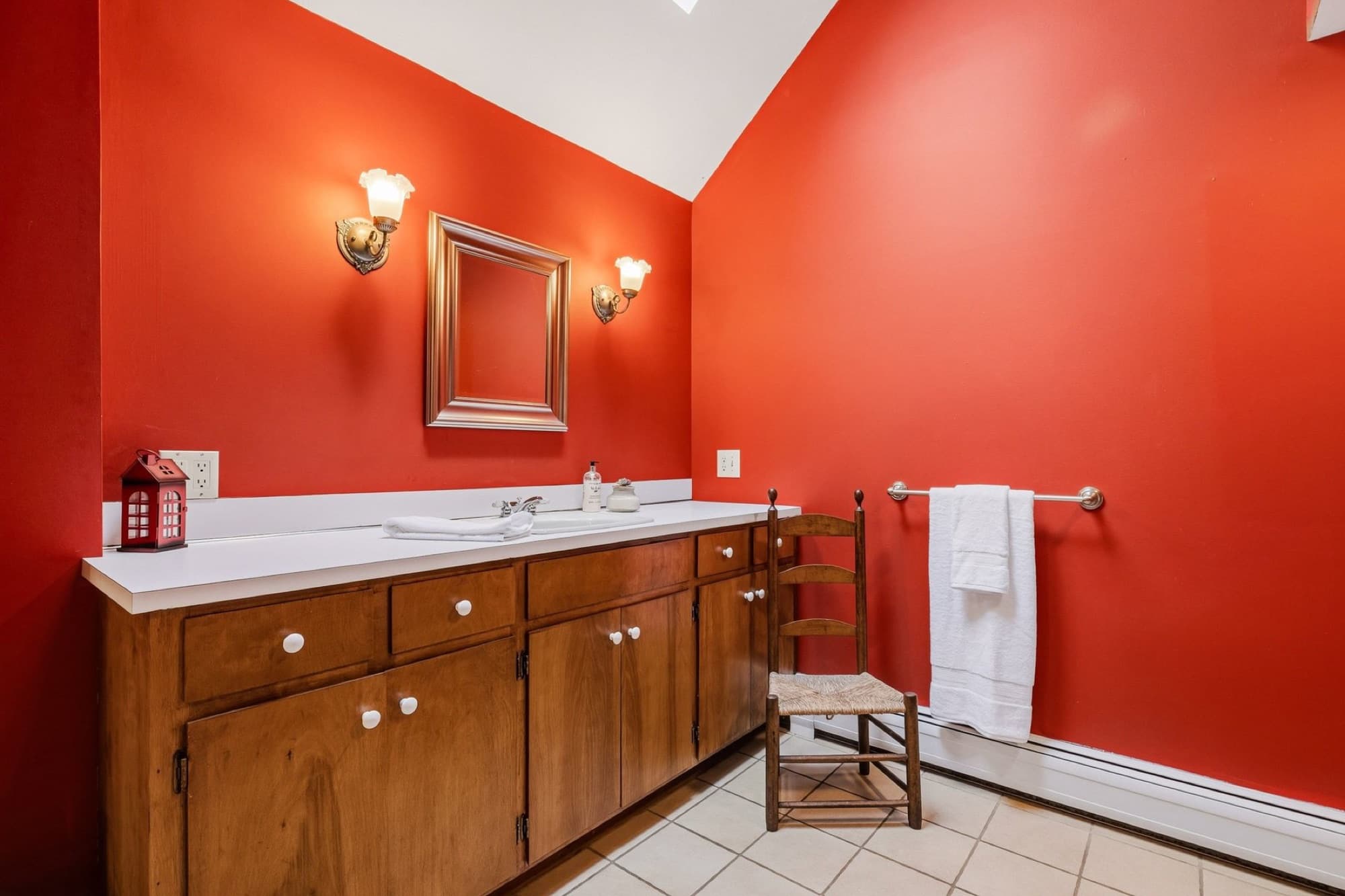 The main-level full bath with red walls, a vaulted ceiling, and a long wood vanity