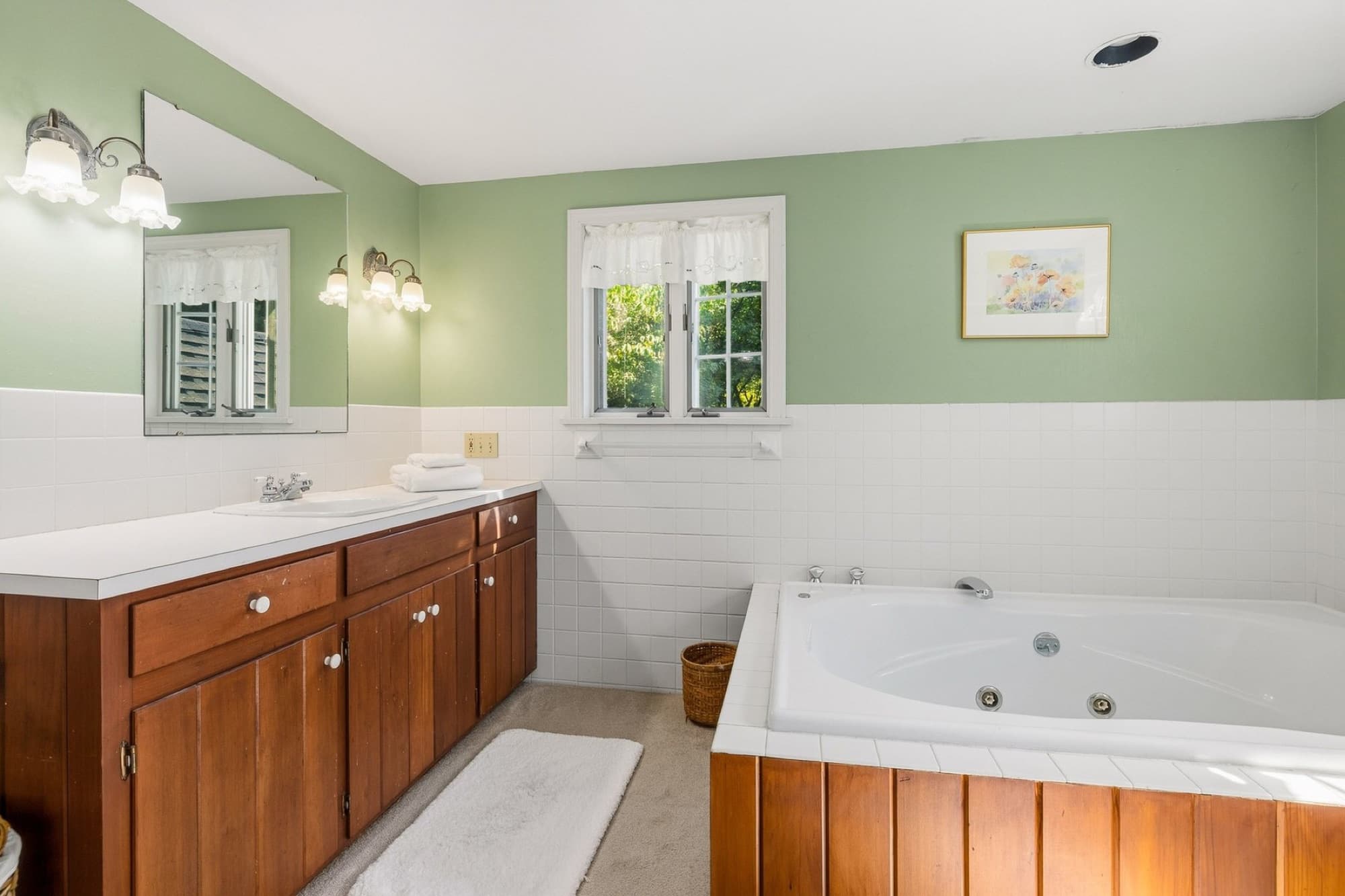 The primary bath with green walls, white tile, a wood vanity, and a whirlpool tub