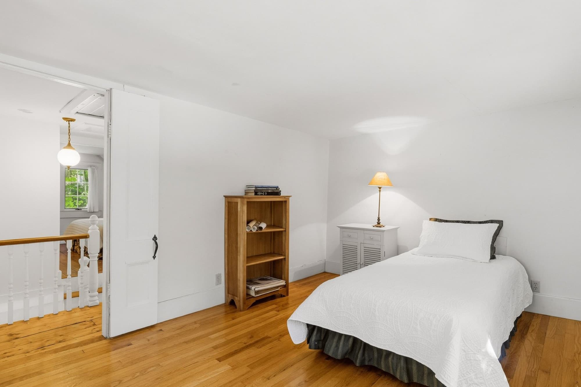 A bedroom with wide-plank floors, a bookcase, and a door to the landing