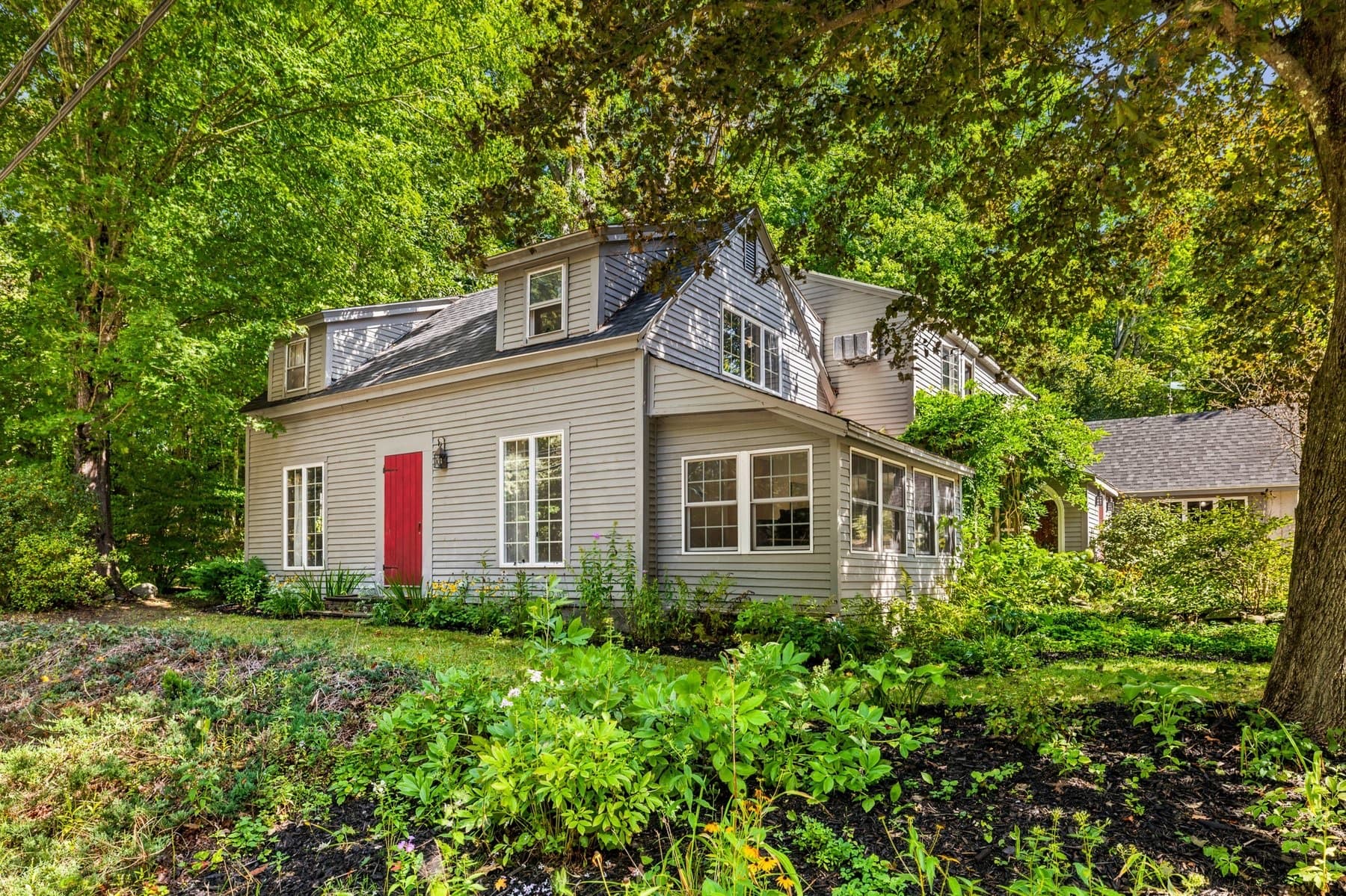 The gray clapboard farmhouse with its red door, seen from the road through the gardens